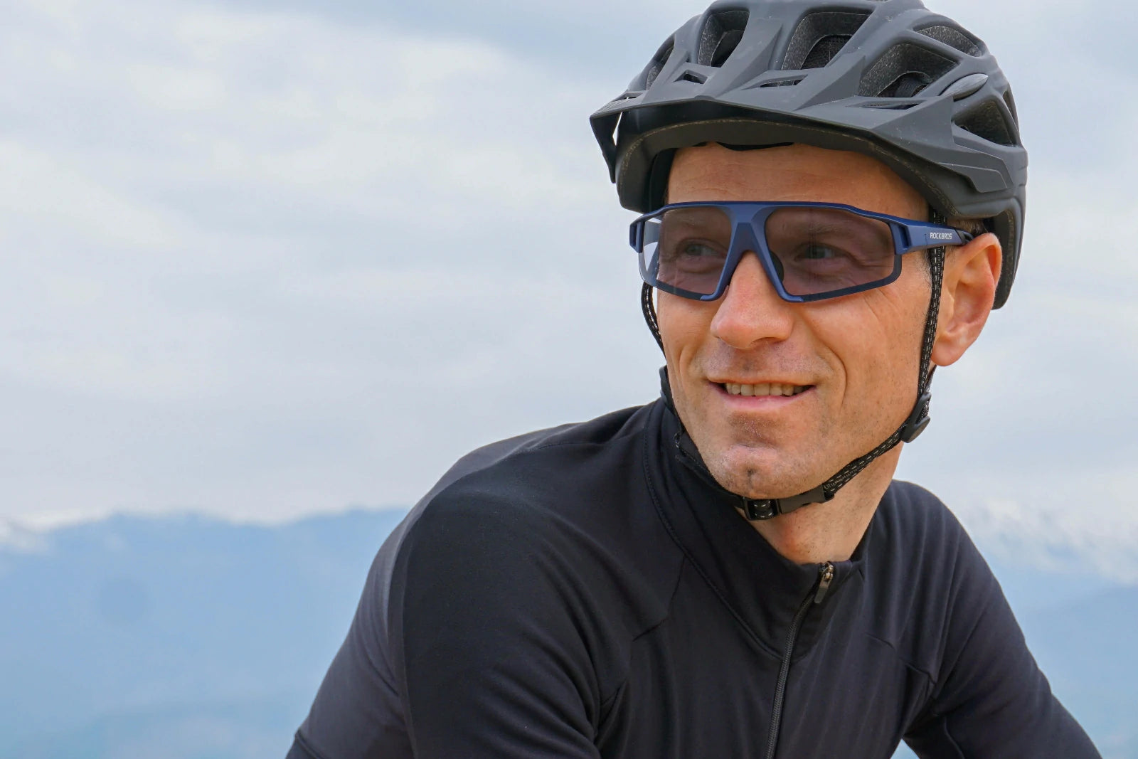 Man wearing a helmet and sunglasses with a mountainous background